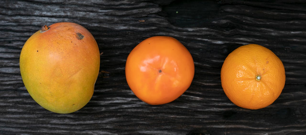 Top view of a mango, persimmon, and orange on a rustic wooden surface. Vibrant and fresh.
