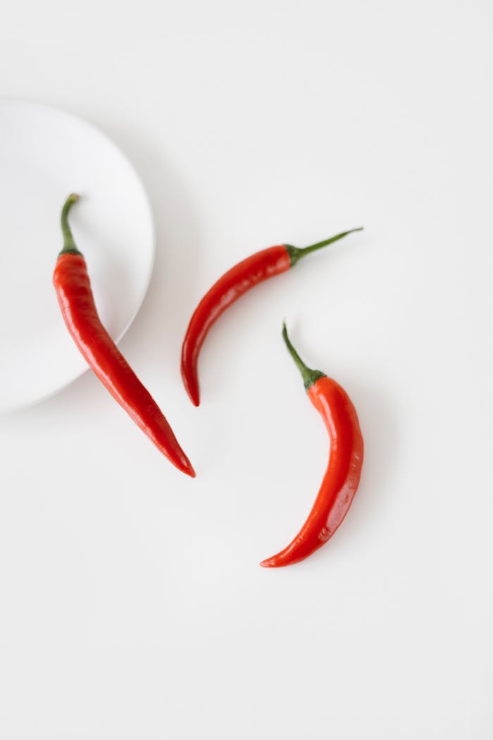 Three vibrant red chili peppers on a minimalist white surface, emphasizing freshness.